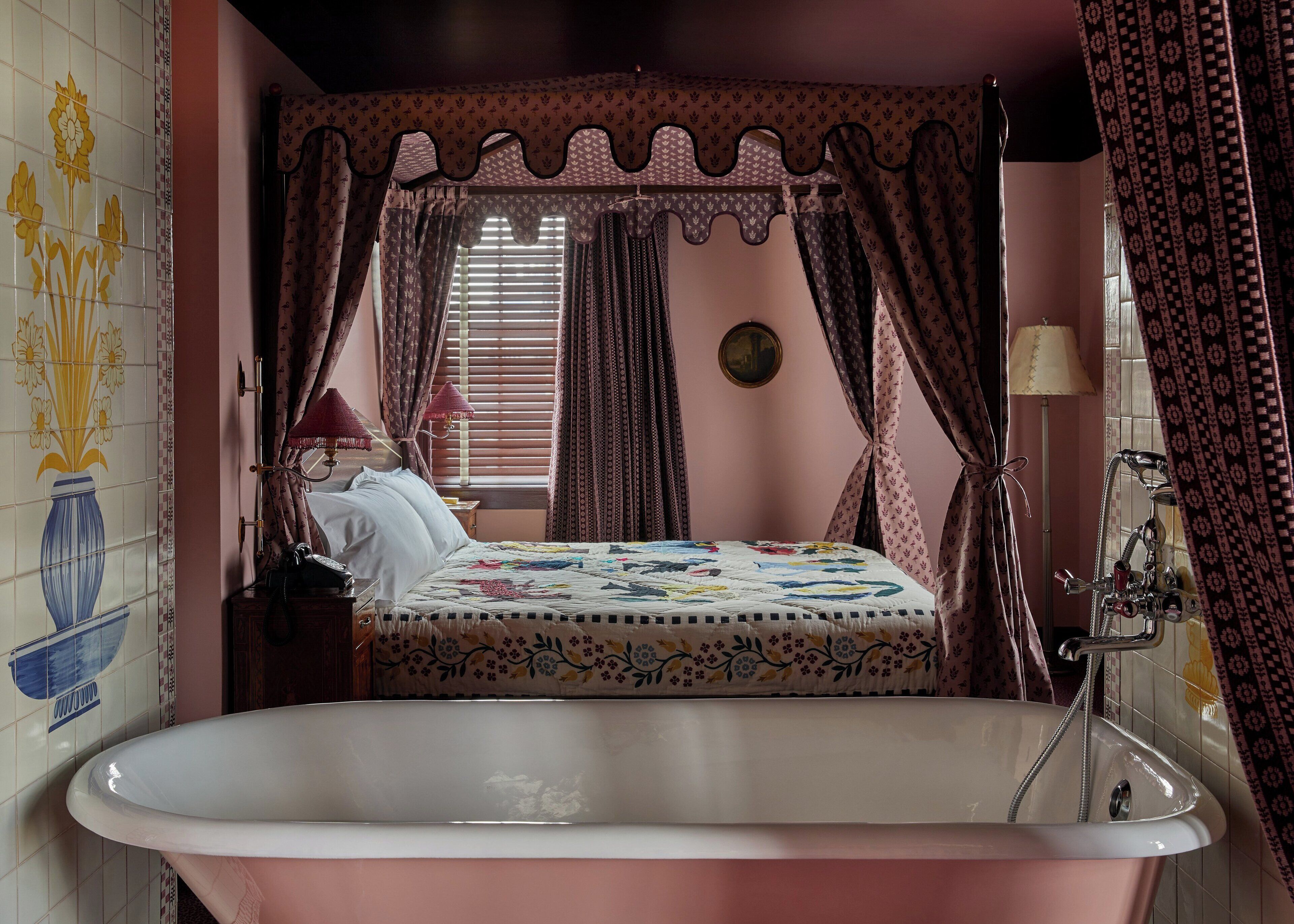 A bedroom with a large bathtub, a bed with a floral bedspread, and a window with curtains.