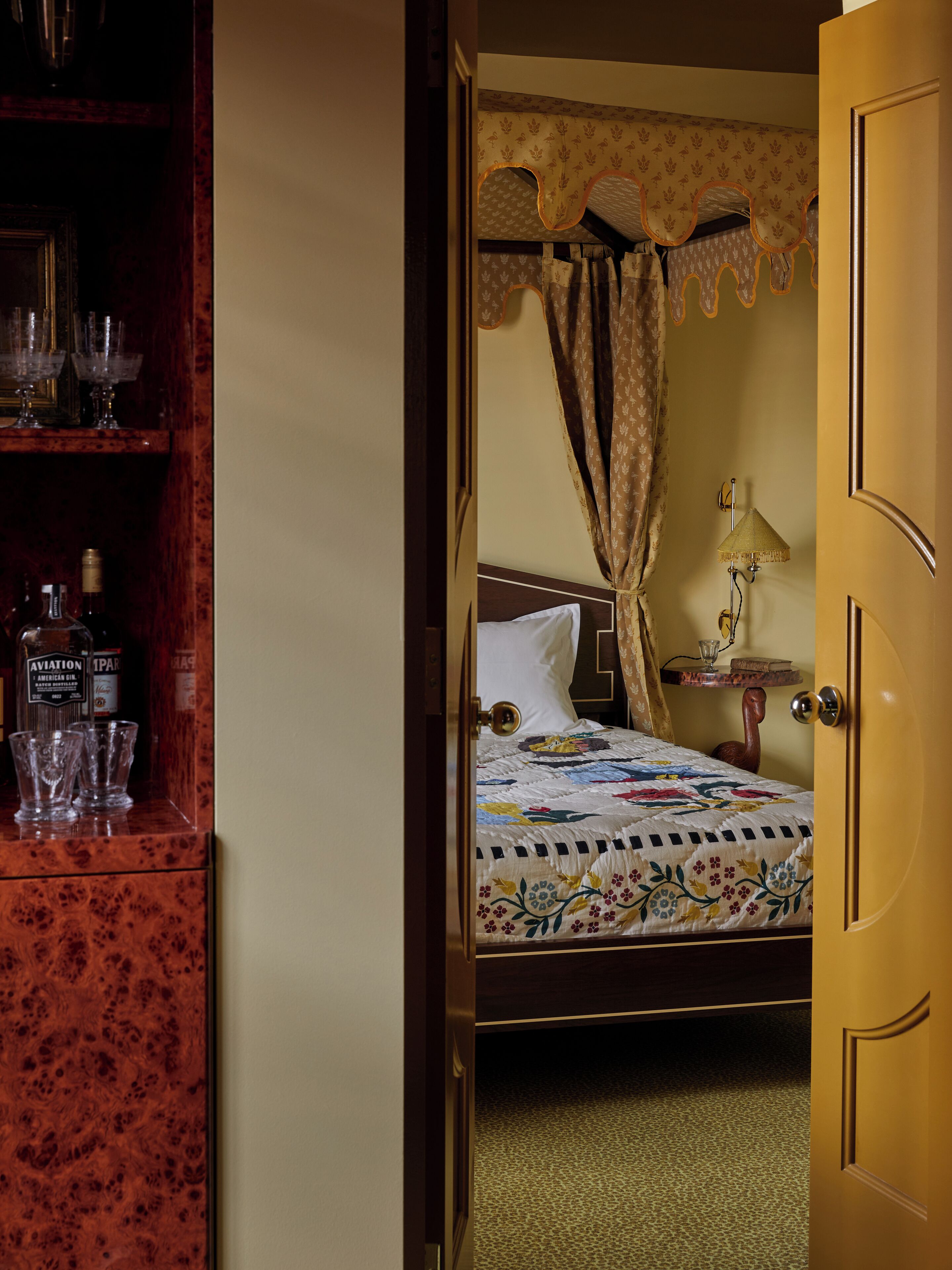 A bedroom with a wooden wardrobe, a bed with a floral quilt, a bedside lamp, and a nightstand with a glass.
