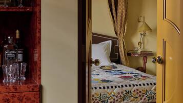 A bedroom with a wooden wardrobe, a bed with a floral quilt, a bedside lamp, and a nightstand with a glass.