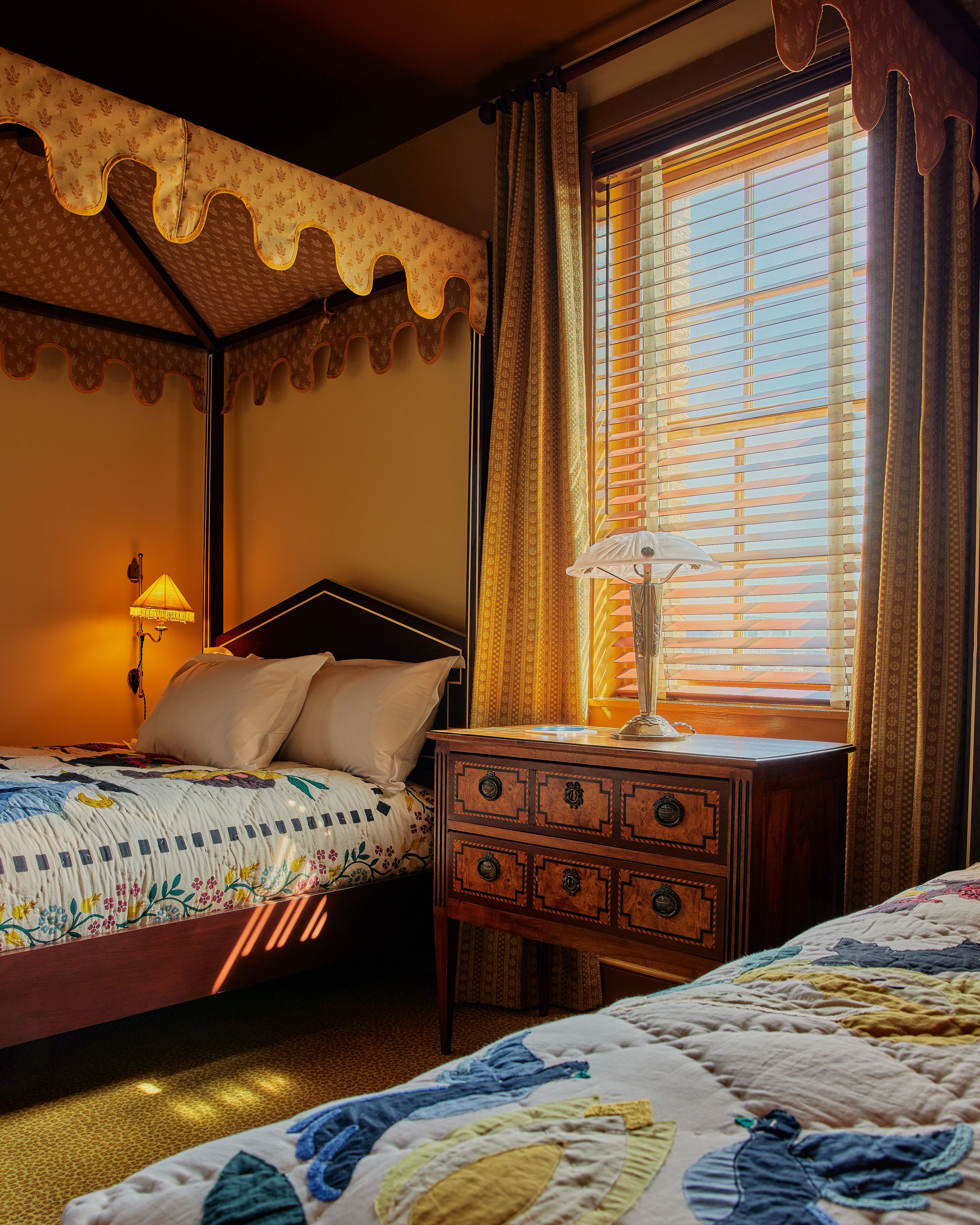 A bedroom with two beds, a nightstand, a lamp, and a window with curtains.