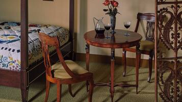 A bedroom with a bed, a wooden chair, a round table with a vase of flowers, and two wine glasses.