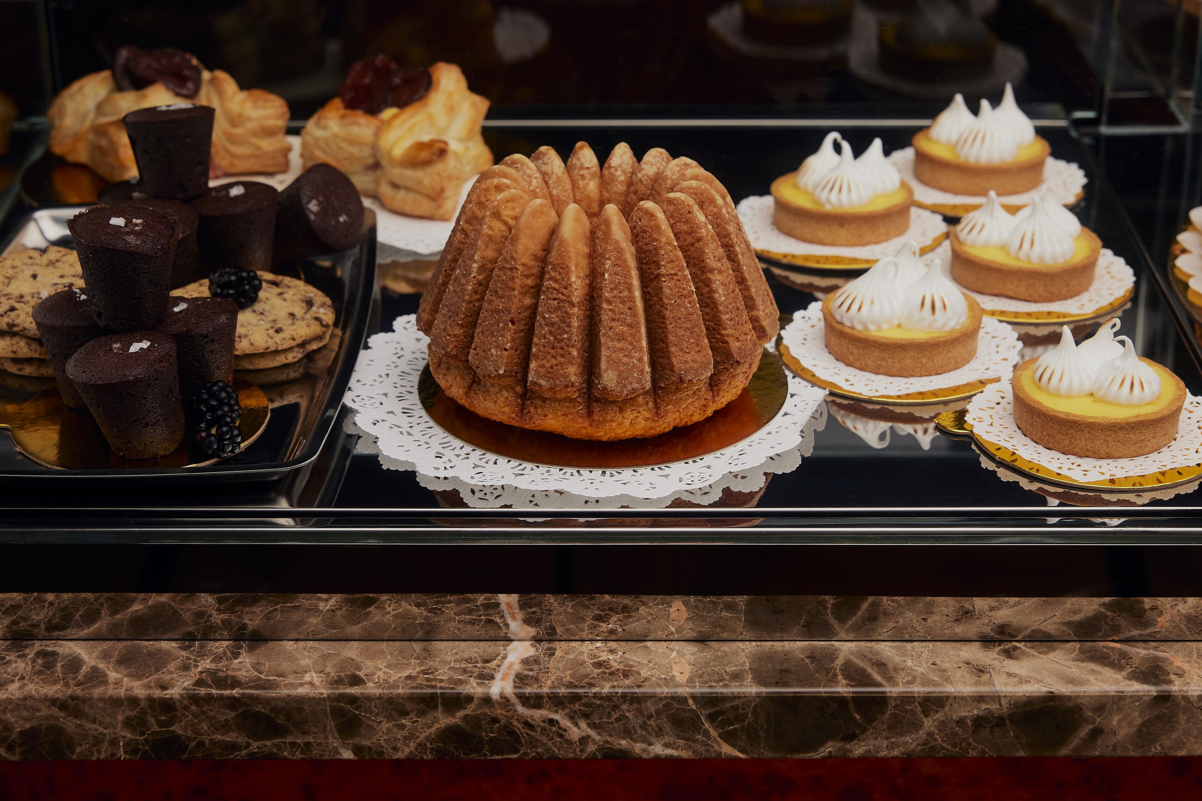 Una exhibición de varios productos horneados, incluyendo un pastel bundt, cupcakes y galletas.