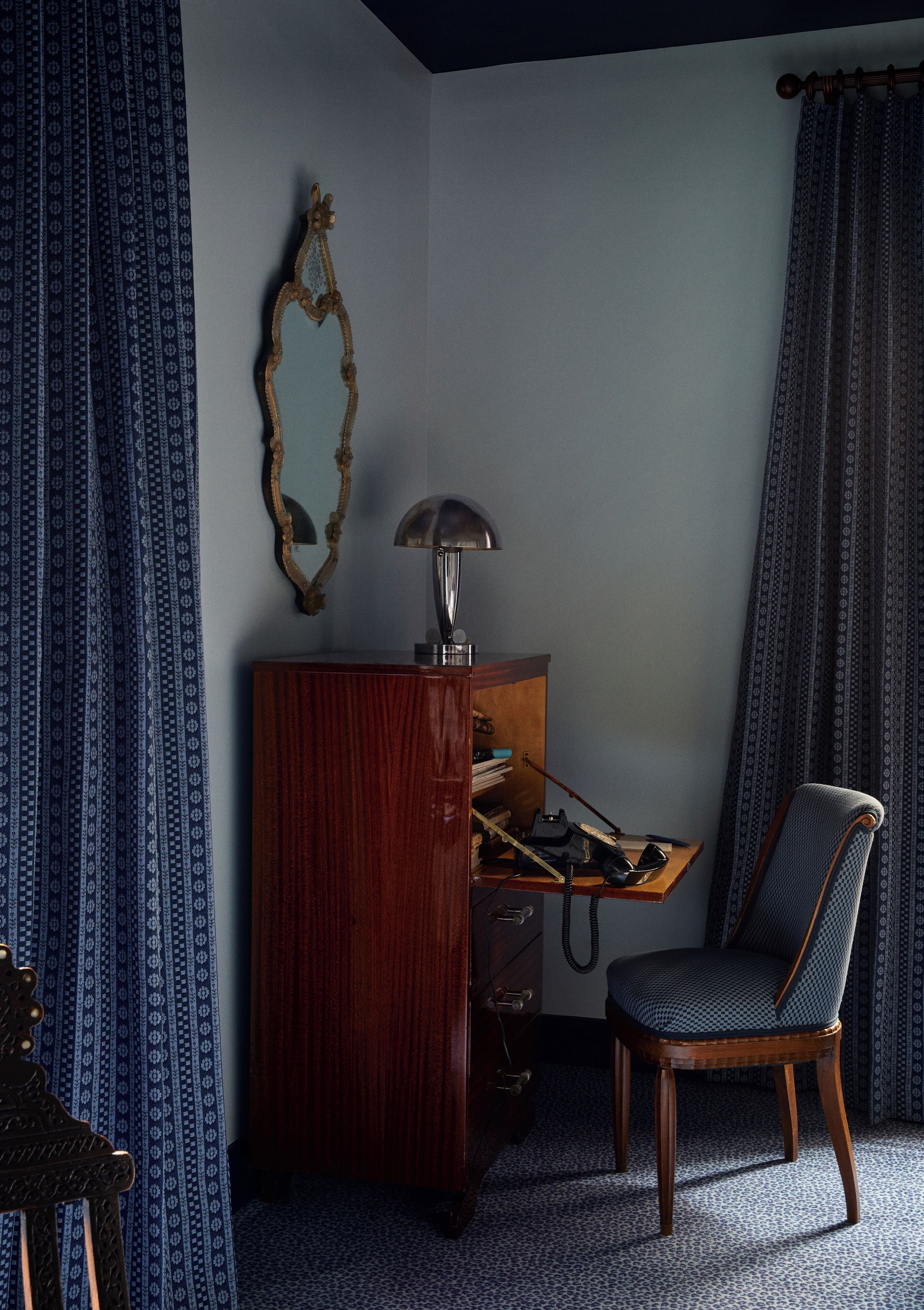 A room with a wooden desk, a chair, a lamp, and a mirror on the wall.