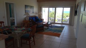 A spacious living area with a glass dining table, wicker furniture, and a view through large sliding glass doors to an outdoor patio. - OCEAN FRONT Conch Shell-Green Turtle Cay with a dock- 15% SUMMER DISCOUNT! (Green Turtle Cay)