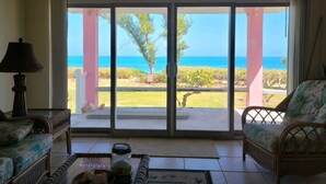 A room with a large sliding glass door leading to a balcony with a view of the ocean. There are two wicker sofas and a table with a lamp and a bottle. - OCEAN FRONT Conch Shell-Green Turtle Cay with a dock- 15% SUMMER DISCOUNT! (Green Turtle Cay)