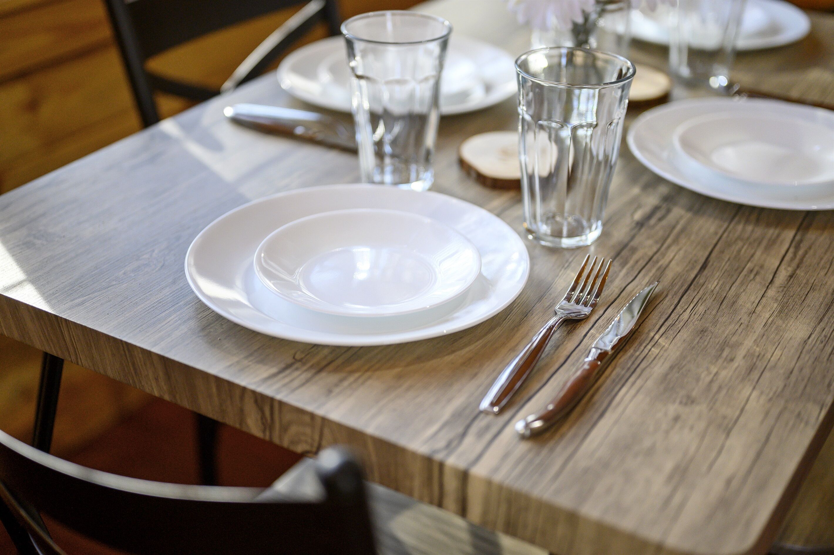 Una mesa de madera con platos blancos, vasos transparentes y cubiertos.