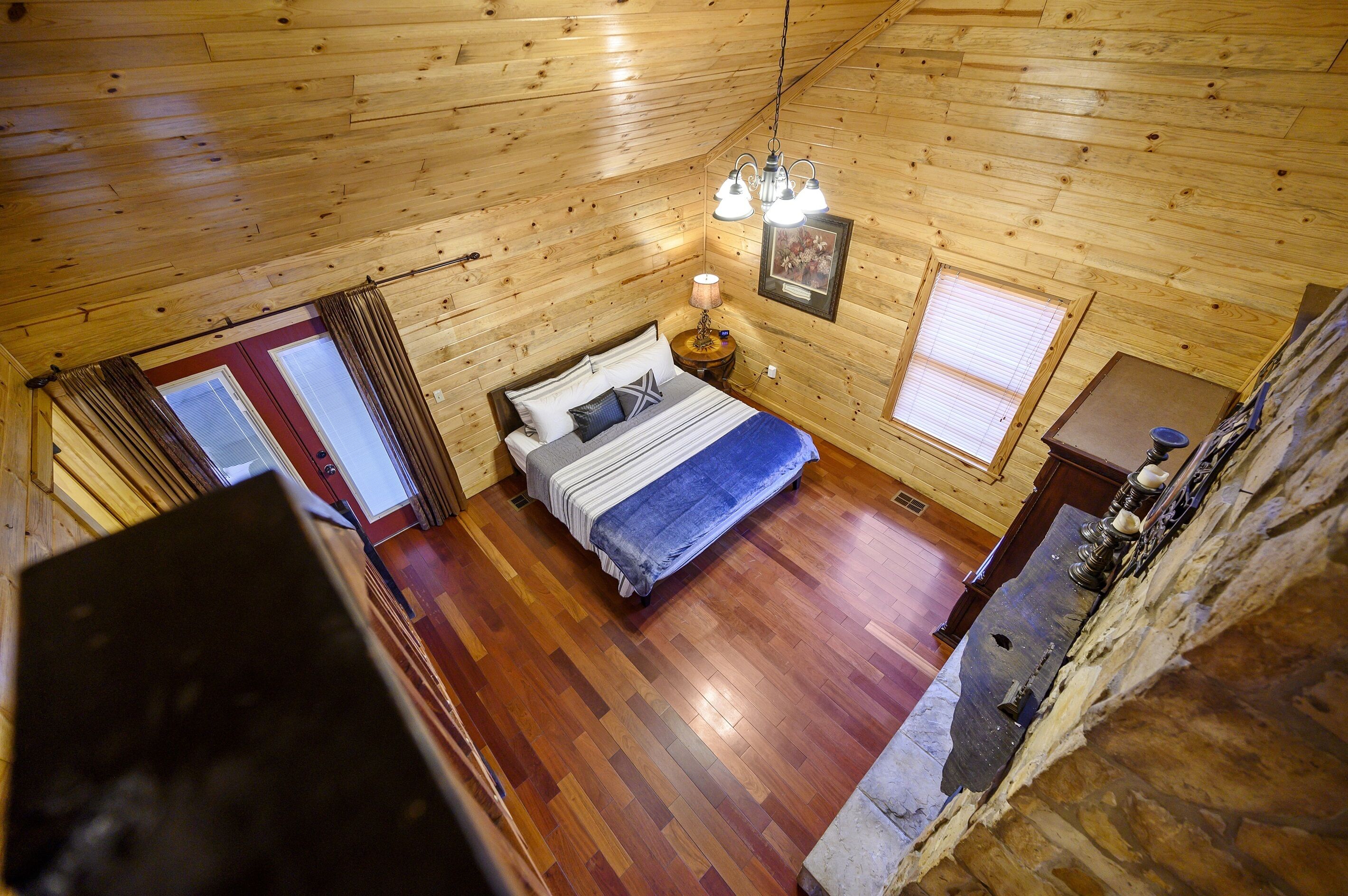 A wooden-paneled bedroom with a bed, bedside lamp, and a framed picture on the wall.