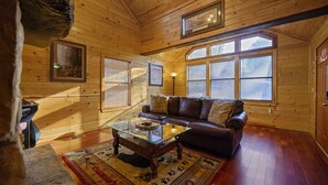 L’intérieur d’une cabane en rondins, avec un plancher en bois, une table basse en verre, un canapé en cuir et un tableau encadré accroché au mur.
