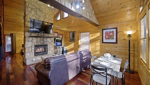 L’intérieur chaleureux d’un chalet avec une cheminée en pierre, des murs en bois, un canapé en cuir et un coin repas.