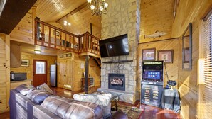 L’intérieur d’un chalet confortable, avec une cheminée en pierre, un canapé en cuir et un téléviseur fixé au mur.
