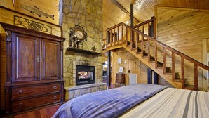 Un intérieur en bois avec une cheminée, un lit recouvert d’une couverture à rayures et un escalier en bois.