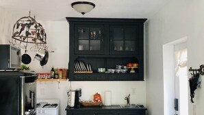A compact kitchen with a black cabinet, a white refrigerator, and a hanging pot rack. - The Cozy Cottage at Cocoa Village-Private Oasis (Cocoa)