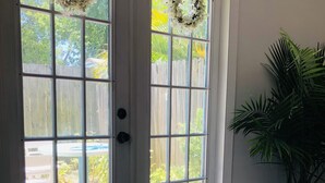 A room with a large sliding glass door leading to a backyard, a potted plant, and a light-colored wooden floor. - The Cozy Cottage at Cocoa Village-Private Oasis (Cocoa)