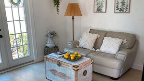 A living room with a beige sofa, a wicker coffee table with fruit, a floor lamp, and a door with a wreath. - The Cozy Cottage at Cocoa Village-Private Oasis (Cocoa)