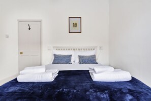 A neatly made bed with white and blue patterned pillows, a dark blue blanket, and two folded white towels.