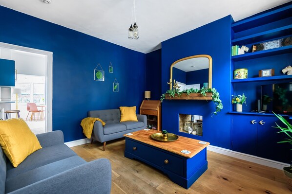 A room with blue walls, a grey sofa with yellow cushions, a wooden coffee table, and a mirror above a fireplace.
