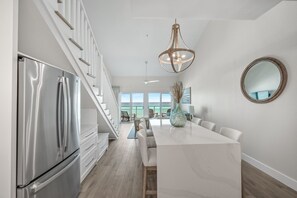 A modern kitchen with a stainless steel refrigerator, a marble island, and a large pendant light.
