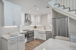 A modern kitchen with white cabinetry, stainless steel appliances, and a marble countertop.