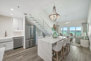 A modern kitchen with white cabinetry, a stainless steel refrigerator, and a large island with bar stools.
