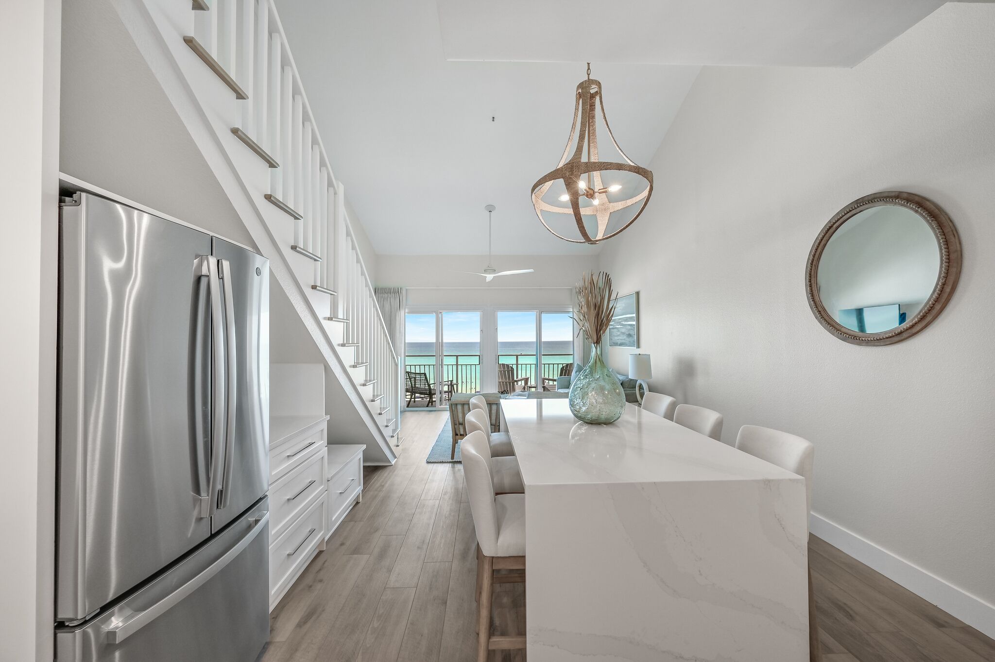 A modern kitchen with a stainless steel refrigerator, a marble island, and a large pendant light.