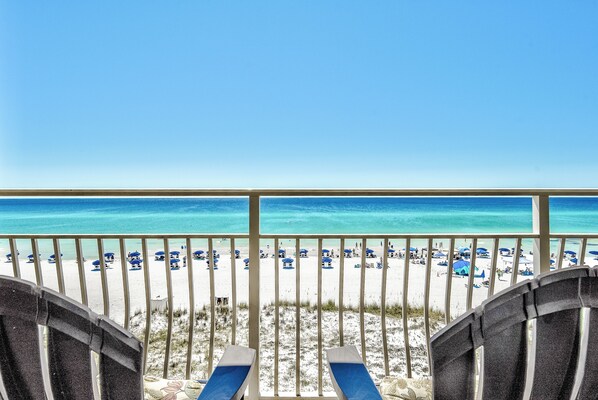 A beach view from a balcony with lounge chairs and umbrellas.