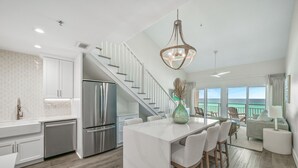 A modern kitchen with white cabinetry, a stainless steel refrigerator, and a large island with bar stools. - Crystal Sands 312B. Completely Renovated Stunner, Free Beach Service, Pool. (Destin)