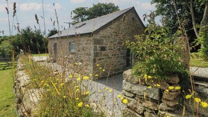 A stone building with a sloped roof, surrounded by natural vegetation and a gravel path. - The Reading Room (Falmouth)