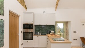 A compact kitchen with white cabinets, a built-in oven, and a green-tiled backsplash. - The Reading Room (Falmouth)