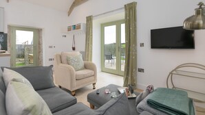 A spacious living room with a sofa, armchair, and a TV mounted on the wall. - The Reading Room (Falmouth)