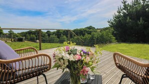 A wooden deck with wicker chairs and a table with a vase of flowers. - The Reading Room (Falmouth)