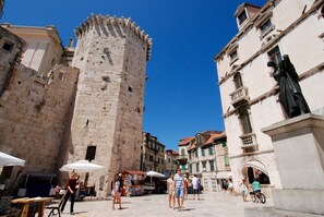 Un'antica torre in pietra e edifici con una piazza lastricata, posti a sedere all'aperto e una statua.