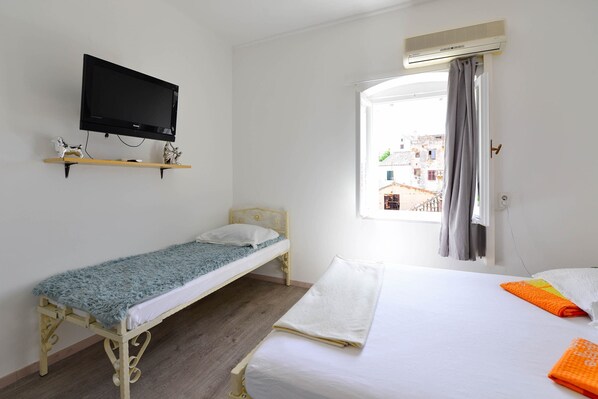 A single bed with a white mattress and a blue blanket, a smaller single bed with a white mattress and a blue blanket, a television mounted on the wall, and a window with curtains. - A2 - Apartment in the Very Heart of Split (Split)