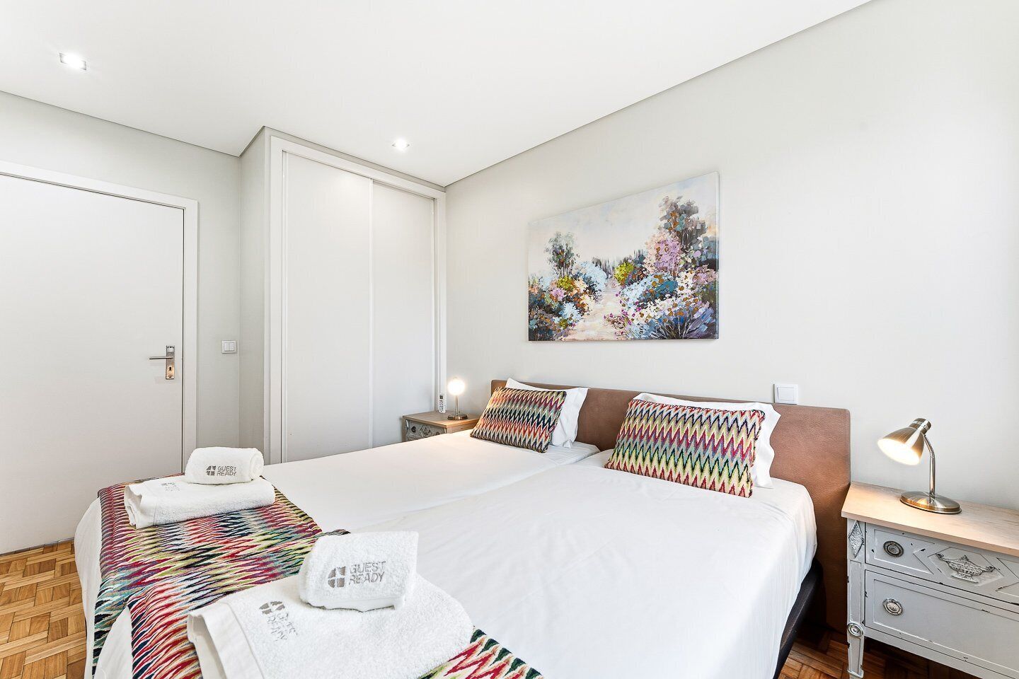 Een moderne hotelkamer met een groot bed, twee nachtkastjes, een schilderij aan de muur en een deur.
