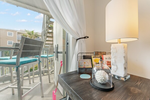 A balcony with white chairs and a table with a lamp, books, and a decorative item. - Ocean View; Fast Beach Access; Pool; Family-Sized Villa; Ideal Spot! (Pensacola Beach)