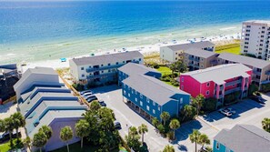 A coastal hotel with multiple buildings, a parking lot, and a beach in the background.