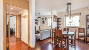 A modern living room with a dining area, wooden flooring, and a large window providing natural light. - GuestReady - Broken Record with Balcony + Parking (Porto)