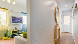 A modern hotel room with a TV, a wooden door, a mirror, and a hallway with a wooden floor. - GuestReady Essential - Heartbeats (Porto)