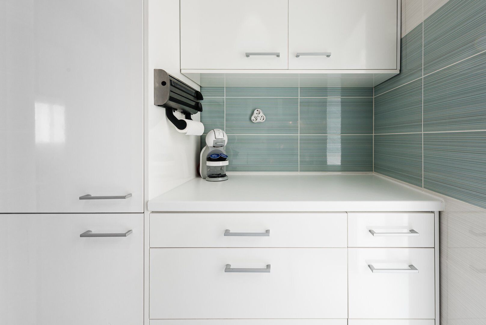 A modern kitchen with white cabinetry, a coffee machine, and a tiled backsplash.