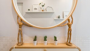 A bathroom with a wooden vanity, a round mirror, and three potted plants on the counter. - GuestReady Essential - Heartbeats (Porto)
