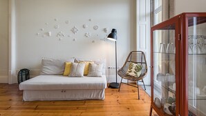Et soveværelse med seng, en gulvlampe, en fletstol og et glaskabinet med pynteting.