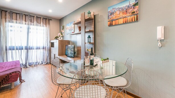 A modern living room with a glass dining table, metal chairs, a sofa, and a TV on a wooden stand. - GuestReady - Sound of Nature - T1 Boavista (Porto)