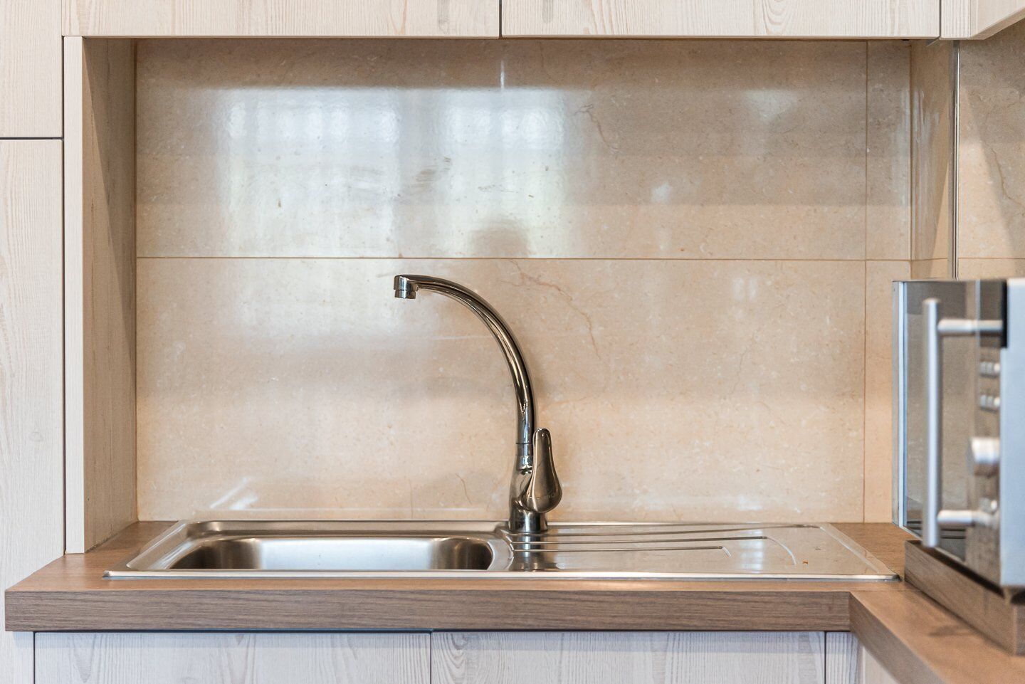 A modern kitchen with a stainless steel sink, wooden cabinets, and a marble backsplash.