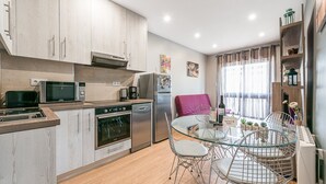 A modern kitchen with stainless steel appliances, a dining area with wire chairs, and a window with curtains. - GuestReady - Sound of Nature - T1 Boavista (Porto)