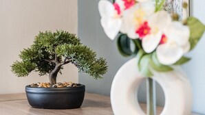 A bonsai tree in a black pot on a wooden surface, next to a white vase with flowers. - GuestReady - Sound of Nature - T1 Boavista (Porto)