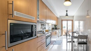 A modern kitchen with wooden cabinets, stainless steel appliances, and a dining area with a glass table and chairs. - GuestReady - Luxe living by the pool (Póvoa de Varzim)