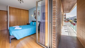 A modern bedroom with a large bed, a sliding glass door to a balcony, and a wooden ceiling. - GuestReady - Luxe living by the pool (Póvoa de Varzim)