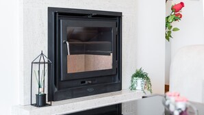 A modern fireplace with a glass door, a small potted plant, and a decorative metal lantern on the mantel. - GuestReady - Luxe living by the pool (Póvoa de Varzim)