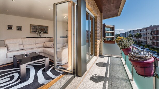 A modern living room with a sofa, coffee table, and a glass door leading to a balcony with potted plants. - GuestReady - Luxe living by the pool (Póvoa de Varzim)