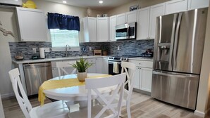 Una cocina moderna con armarios blancos, electrodomésticos de acero inoxidable, una mesa redonda con sillas blancas y una planta en maceta sobre la mesa.