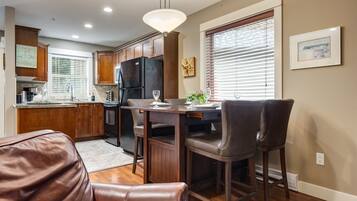 A modern kitchen with dark wooden cabinets, a black refrigerator, and a dining area with two leather chairs and a table.